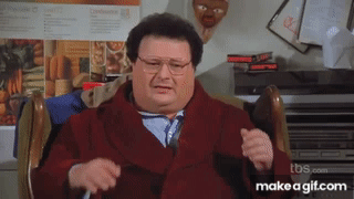 A Man In A Red Coat And Tie Is Sitting In A Chair .. GIF