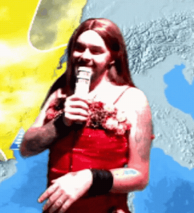 A Man In A Red Dress Is Holding A Microphone In His Hand GIF