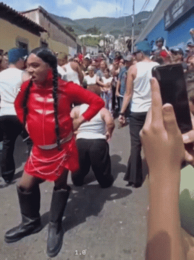 A Man In A Red Dress Is Kneeling Down In Front Of A Crowd While Someone Takes A Picture Of Him GIF
