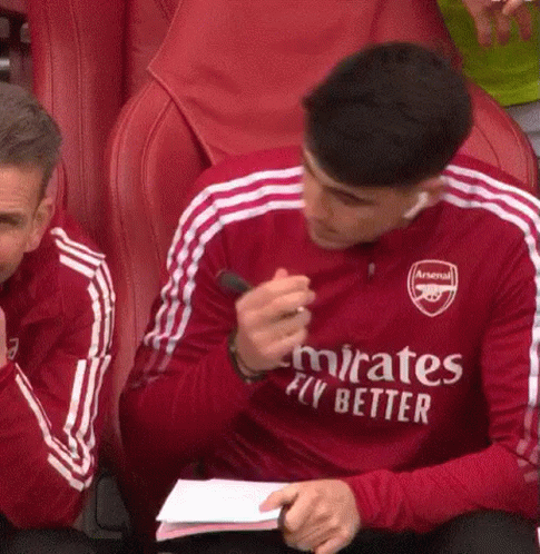 A Man In A Red Emirates Fly Better Jersey Is Sitting In A Red Chair Holding A Pen . GIF