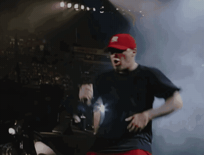 A Man In A Red Hat And Black Shirt Is Dancing On A Stage GIF