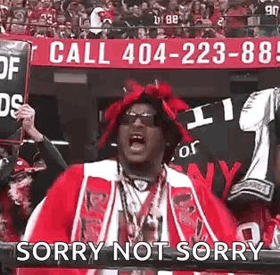 A Man In A Red Hat Is Holding A Sign That Says `` Sorry Not Sorry '' In Front Of A Crowd Of People . GIF