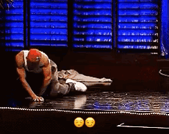 A Man In A Red Hat Is Kneeling Down On A Stage In A Dark Room . GIF