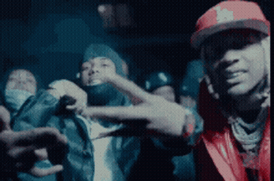 A Man In A Red Hat Is Making A Peace Sign In Front Of A Group Of People . GIF