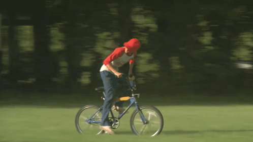 A Man In A Red Hat Is Riding A Bicycle On A Field GIF