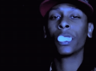 A Man In A Red Hat Is Smoking A Cigarette In The Dark . GIF