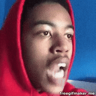 A Man In A Red Hoodie Is Blowing A Bubble In His Mouth GIF