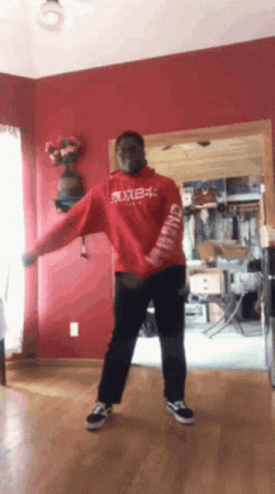 A Man In A Red Hoodie Is Dancing In A Living Room With A Red Wall GIF