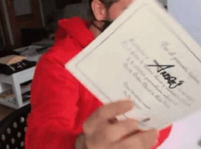 A Man In A Red Hoodie Is Holding A Piece Of Paper With The Name Angel Written On It GIF