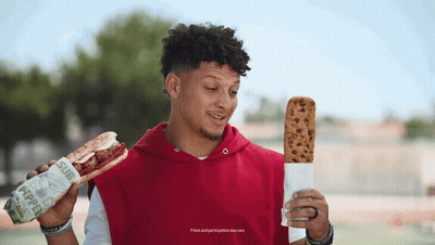 A Man In A Red Hoodie Is Holding A Sub Sandwich And A Cookie GIF