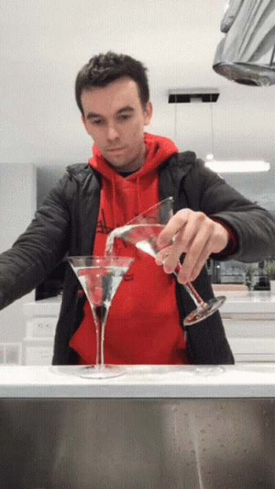 A Man In A Red Hoodie Pours A Martini Into Two Glasses GIF