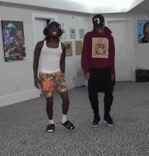 A Man In A Red Hoodie With The Letter C On It Stands Next To Another Man In A White Tank Top GIF