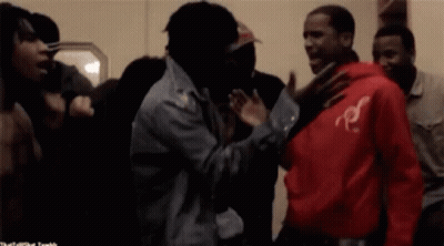 A Man In A Red Hoodie With The Letter R On It Stands In A Crowd Of People GIF