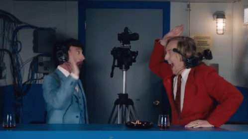 A Man In A Red Jacket And A Man In A Blue Suit Are Sitting At A Counter GIF