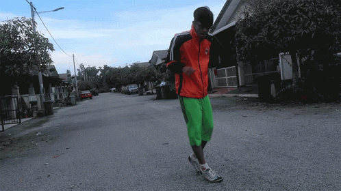 A Man In A Red Jacket And Green Shorts Is Walking Down The Street GIF