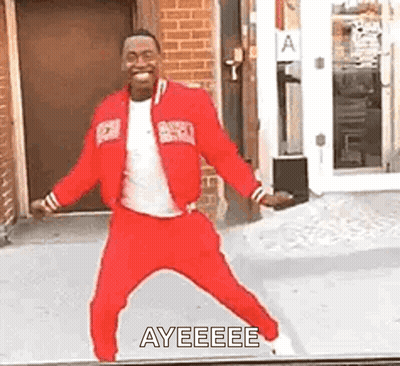 A Man In A Red Jacket And Pants Is Dancing In Front Of A Building . GIF