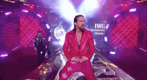 A Man In A Red Jacket And Red Pants Is Standing On A Stage In Front Of A Sign That Says Heavyweight Champion . GIF