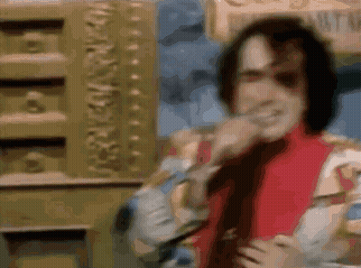 A Man In A Red Jacket And Tie Is Standing In Front Of A Gold Wall And Smiling . GIF