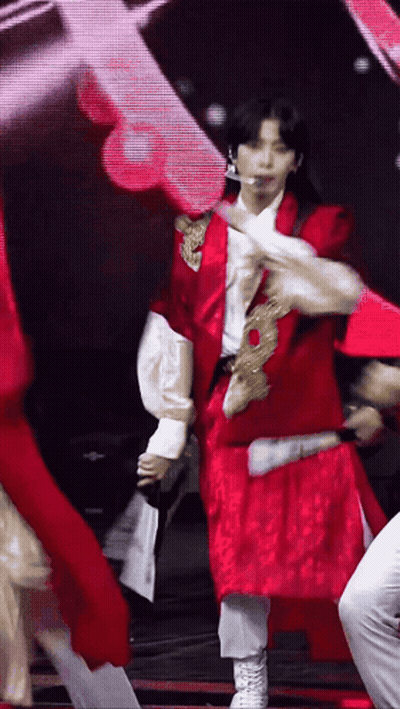 A Man In A Red Jacket And White Pants Is Dancing On A Stage GIF