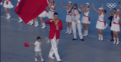 A Man In A Red Jacket Is Carrying A Red Flag And A Boy In A White Shirt Is Holding A Flag GIF