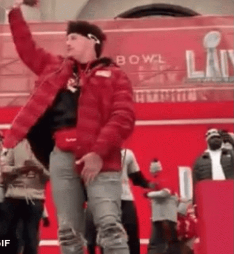 A Man In A Red Jacket Is Dancing In Front Of A Crowd At A Bowl . GIF