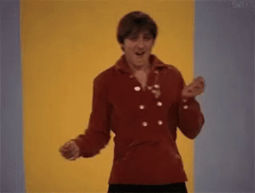 A Man In A Red Jacket Is Dancing In Front Of A Yellow Wall . GIF