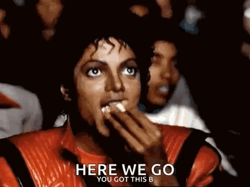 A Man In A Red Jacket Is Eating Popcorn And Says Here We Go You Got This B. GIF