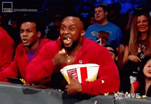 A Man In A Red Jacket Is Eating Popcorn While Watching A Wrestling Show GIF