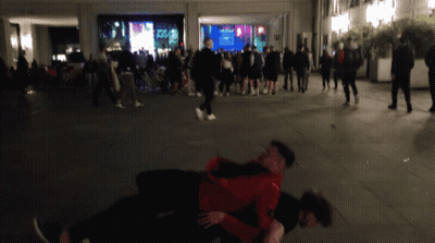 A Man In A Red Jacket Is Holding Another Man In A Crowd GIF