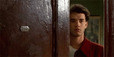 A Man In A Red Jacket Is Peeking Out From Behind A Door . GIF
