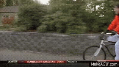 A Man In A Red Jacket Is Riding A Bike Down A Street With A Makeagif.com Link In The Corner GIF