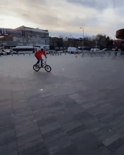 A Man In A Red Jacket Is Riding A Bike On A Concrete Pavement GIF