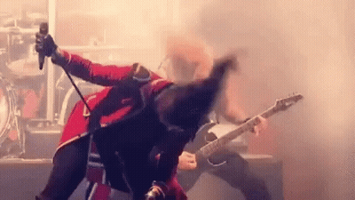 A Man In A Red Jacket Is Singing Into A Microphone While Another Man Plays A Guitar . GIF