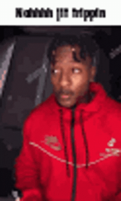 A Man In A Red Jacket Is Sitting In A Car And Looking At The Camera . GIF