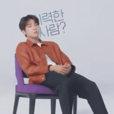 A Man In A Red Jacket Is Sitting In A Chair With His Hands Folded . GIF
