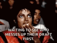 A Man In A Red Jacket Is Sitting In Front Of A Crowd Eating A Sandwich . GIF