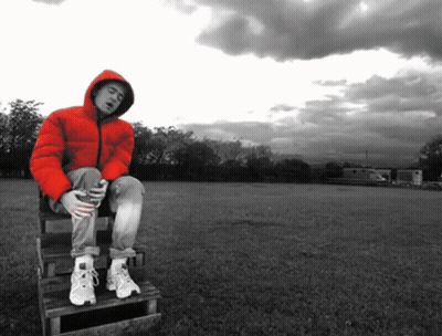 A Man In A Red Jacket Is Sitting On A Wooden Bench In A Field GIF