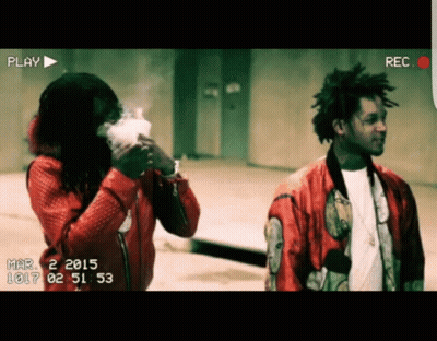 A Man In A Red Jacket Is Smoking A Cigarette While Another Man Looks On GIF