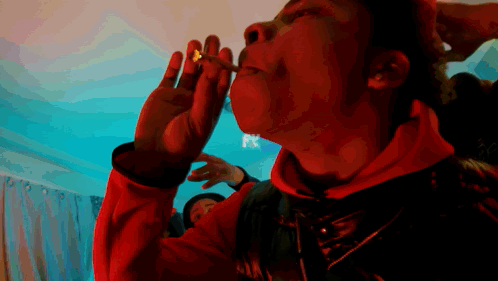 A Man In A Red Jacket Is Smoking A Cigarette With A Fx Logo Behind Him GIF