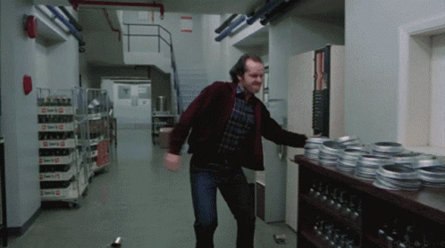 A Man In A Red Jacket Is Standing In A Hallway Next To A Shelf With Rolls Of Film GIF