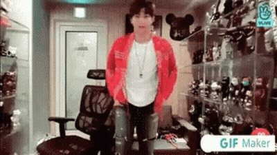 A Man In A Red Jacket Is Standing In A Room With A Chair . GIF