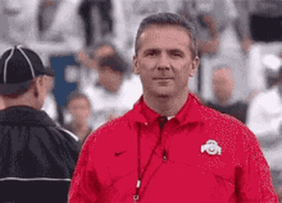 A Man In A Red Jacket Is Standing In A Stadium . GIF