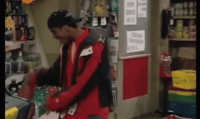 A Man In A Red Jacket Is Standing In A Store Holding A Bottle Of Soda . GIF