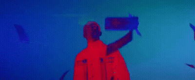 A Man In A Red Jacket Is Standing In Front Of A Blue Background In A Dark Room . GIF