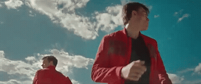 A Man In A Red Jacket Is Standing In Front Of A Blue Sky With Clouds . GIF
