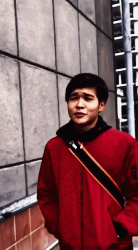 A Man In A Red Jacket Is Standing In Front Of A Building GIF