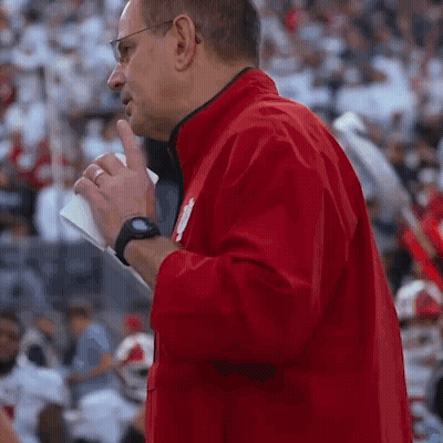 A Man In A Red Jacket Is Standing In Front Of A Crowd Holding A Piece Of Paper GIF