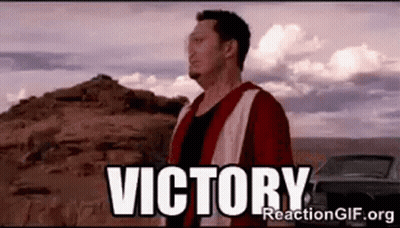 A Man In A Red Jacket Is Standing In Front Of A Mountain With The Word Victory Written On It . GIF