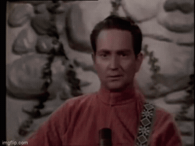A Man In A Red Jacket Is Standing In Front Of A Painting And Holding A Microphone . GIF