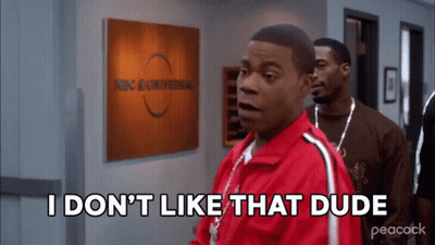 A Man In A Red Jacket Is Standing In Front Of A Sign That Says Nbc Universal GIF